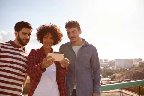 Three young millennials looking at cellphone with smile Stock Photos