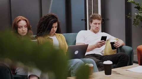 Three young multi ethnic people use or work with different gadgets, with a Stock Footage 263835614