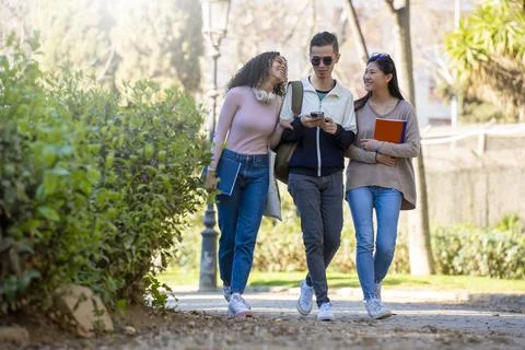 Three young multiethnic students walking in the street and looking at the phone Stock Photos