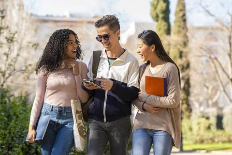 Three young multiethnic students walking in the street and looking at the phone Stock Photos