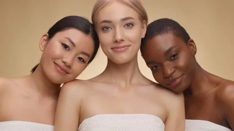Three young multiethnic women posing wrapped in towels over beige studio Stock Footage 154663302