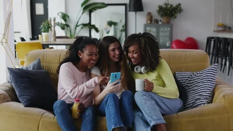 Three young multiracial women using mobile phone while relaxing together at home Stock Footage 283034383