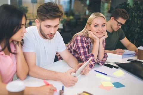 Three young peoople work seriously at table. They look down. Young blonde woman Foto stock