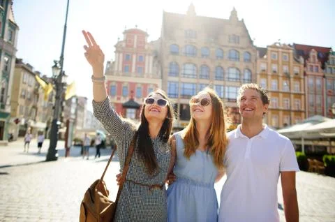 Three young people stand on the square of the ancient city. Stock Photos