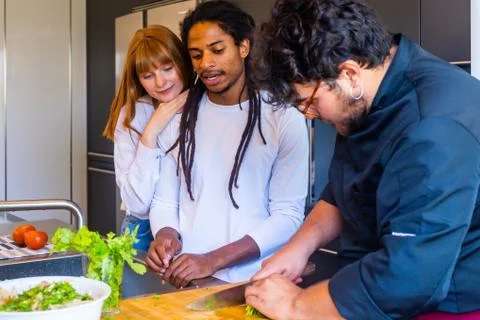 Three young people talking while cooking Stock Photos