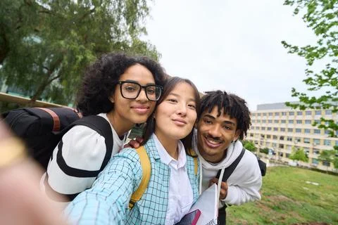 Three young students are posing for a picture in front of a building - selfie Stock Photos