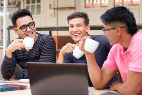 Three young students drinking coffee outdoors while talking and laughing. Foto stock