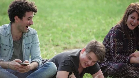 Three Young students relax on the lawn chatting, laughing and relaxing in a park 스톡 동영상 76450256