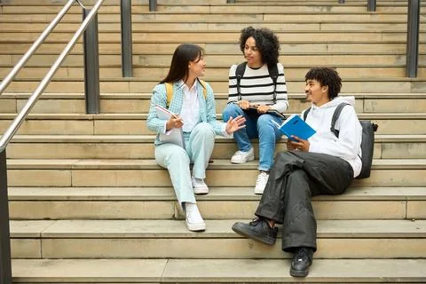 Three young students sitting on steps, one of them reading a book Stock Photos
