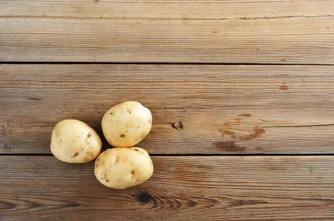 Three young tuber raw white potatoes on rustic wooden background Stock Photos