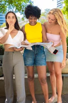 Three young women checking a map while planning their trip outdoors Stock Photos