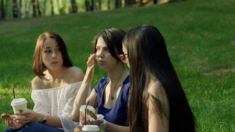 Three young women drinking drinks and eating pastries in a summer park. 4K Stock Footage 87921874