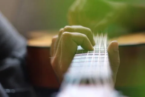 Through the cut-outs of a monstera leaf, hands can be seen playing chords a.. Stock Photos