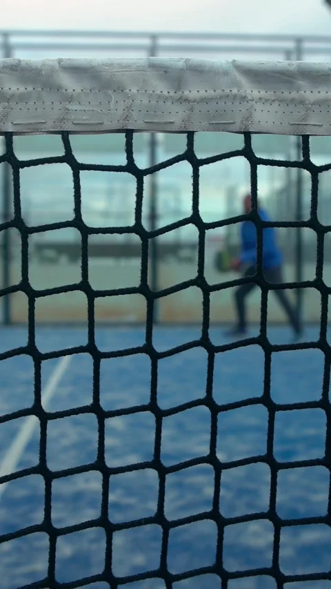 Through grid view of paddle tennis man playing on blue court outdoors. Sport Stock Footage 312951546