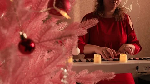 Through the pink Christmas tree, you can see a woman playing the white piano Stock Footage 325526693