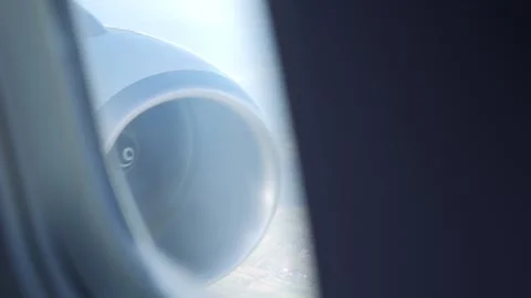 Through the planes window, the jet engine spins steadily as clouds drift by.. Stock Footage 290087643