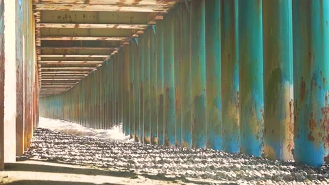 Through the rusty columns from the bridge beat the waves on the rocky beach Stock Footage 171147923