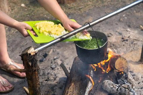 Throw the ingredients into the soup which is cooked over a fire in a pot Stock-Fotos