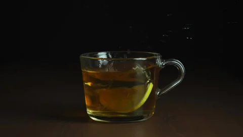Throw slice of lemon with splash into a glass mug with tea on a dark background Stock Footage 168735049