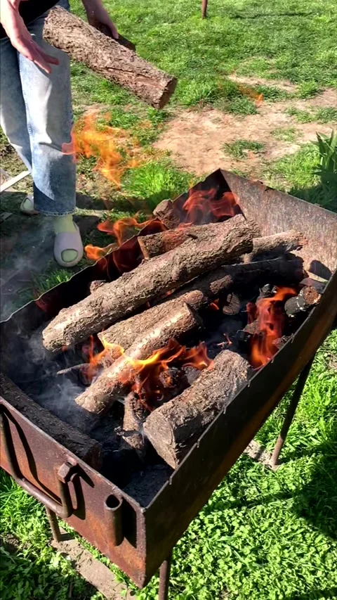 Throwing firewood into a burning metal grill outdoors. Stock Footage 339972859