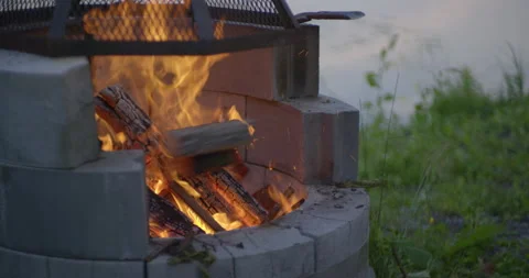 Throwing a log in campfire pit by the lake at evening in slow motion Stock Footage 130927655