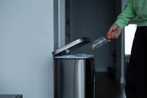 Throwing a plastic bottle into a large metal trash can. Sorting garbage at home. Stock Photos