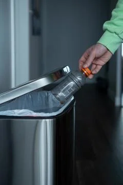 Throwing a plastic bottle into a large metal trash can. Sorting garbage at home. Stock Photos