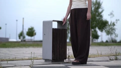 Throws empty plastic water bottle into outdoor metal and wood trash bin  Stock Footage 341409918