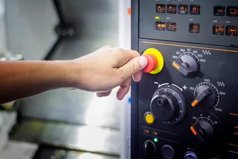 A Thumb ready to press emergency Stop button on Control panel of CNC machine Stock Photos