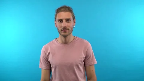 Thumbs up! contented attractive long-haired male rocker over isolated blue Stock Footage 137457988