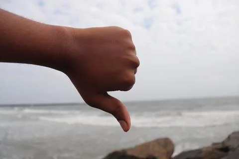 Thumbs Down Hand Gesture Against Sea and Beach Background Stock Photos