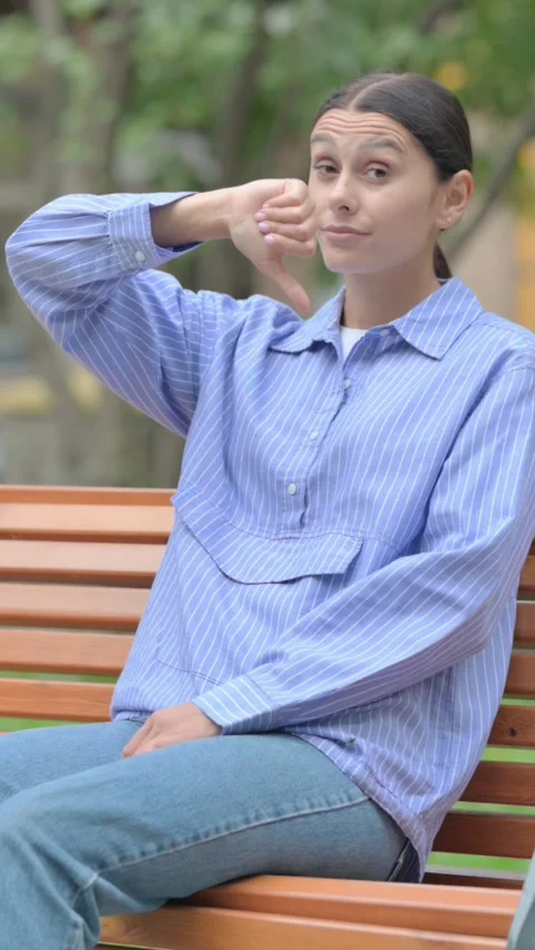 Thumbs Down by Hispanic Woman while Sititng Outdoor, vertical Stock-Footage 321121713
