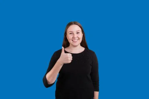 Thumbs up given by young women on solid blue backdrop Stock Photos