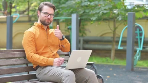 Thumbs Up by Man in Glasses Using Laptop Outdoor on Bench 動画素材 282431892