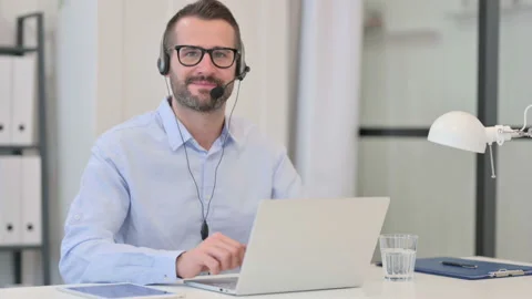 Thumbs Up by Middle Aged Man with Headset while using Laptop Stock Footage 145401396