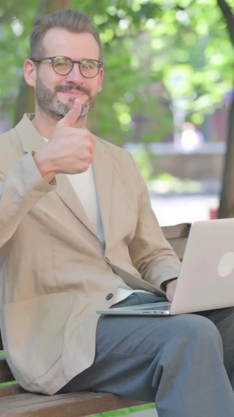 Thumbs Up by Middle Aged Man with Laptop Sitting Outdoor on Bench, Vertical Stock Footage 319014204