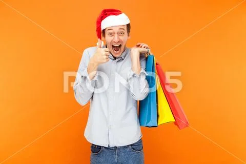 Thumbs up, like sign. Man shopaholic in red cap, holding many colorful bags a Stock Photos