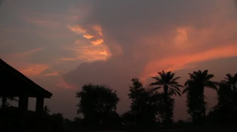 Thunderhead builds over palm trees with African villagers Stock Footage 21523740