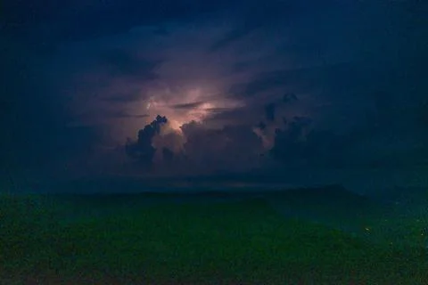 Thunderstorm cloud glowing over dark hills at night Stock Photos