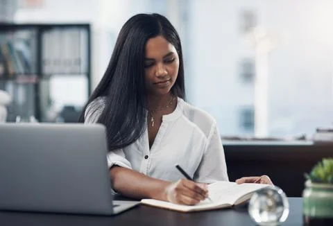 Ticking off tasks from her to-do list. a young businesswoman writing notes while Stock Photos