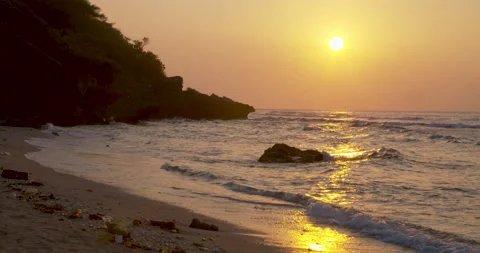 Tidal waves hitting the sandy beach shore during sunset time with mountain in th 動画素材 135967581