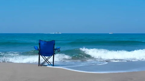 Tide gently approaching a relaxing beach chair on the shoreline Stock Footage 297714051