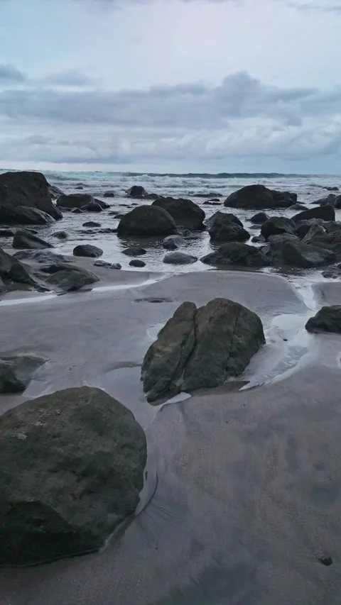 Tide gently lapping over black volcanic rocks on a black sand beach Video stock 294272626