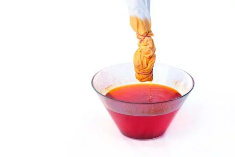 Tie Dye Process with Fabric Dripping into Glass Bowl of Orange Dye Stock Photos