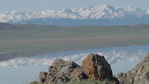 Tien Shan mountains reflected in calm lake with rocks in foreground, layered lan Vidéo 333914014