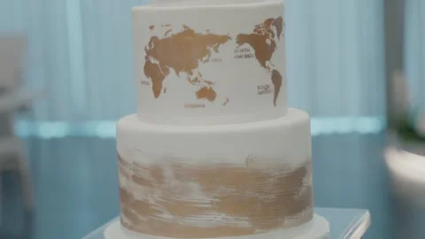 Tiered wedding cake featuring a world map design in gold on white icing Vidéo 289234064