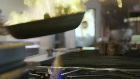 A Tight pan of chef flame sauteing vegetables over stove Stock Footage 155452918