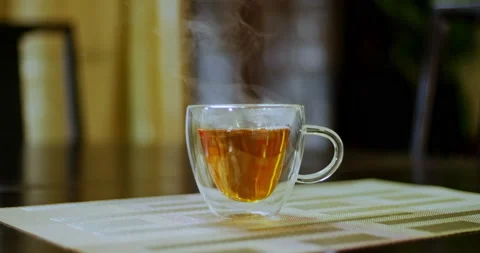Tight shot of hot steaming tea in a transparent glass tea cup on a dining table Stock-Footage 199439860