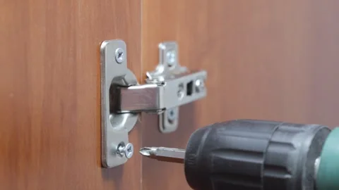 Tighten the screw when installing a door hinge in a wooden cabinet. Video stock 289274593