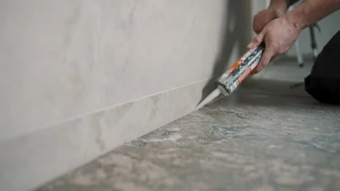 Tile installation by man sealing edges with caulk in a modern home setting Stock Footage 307042060
